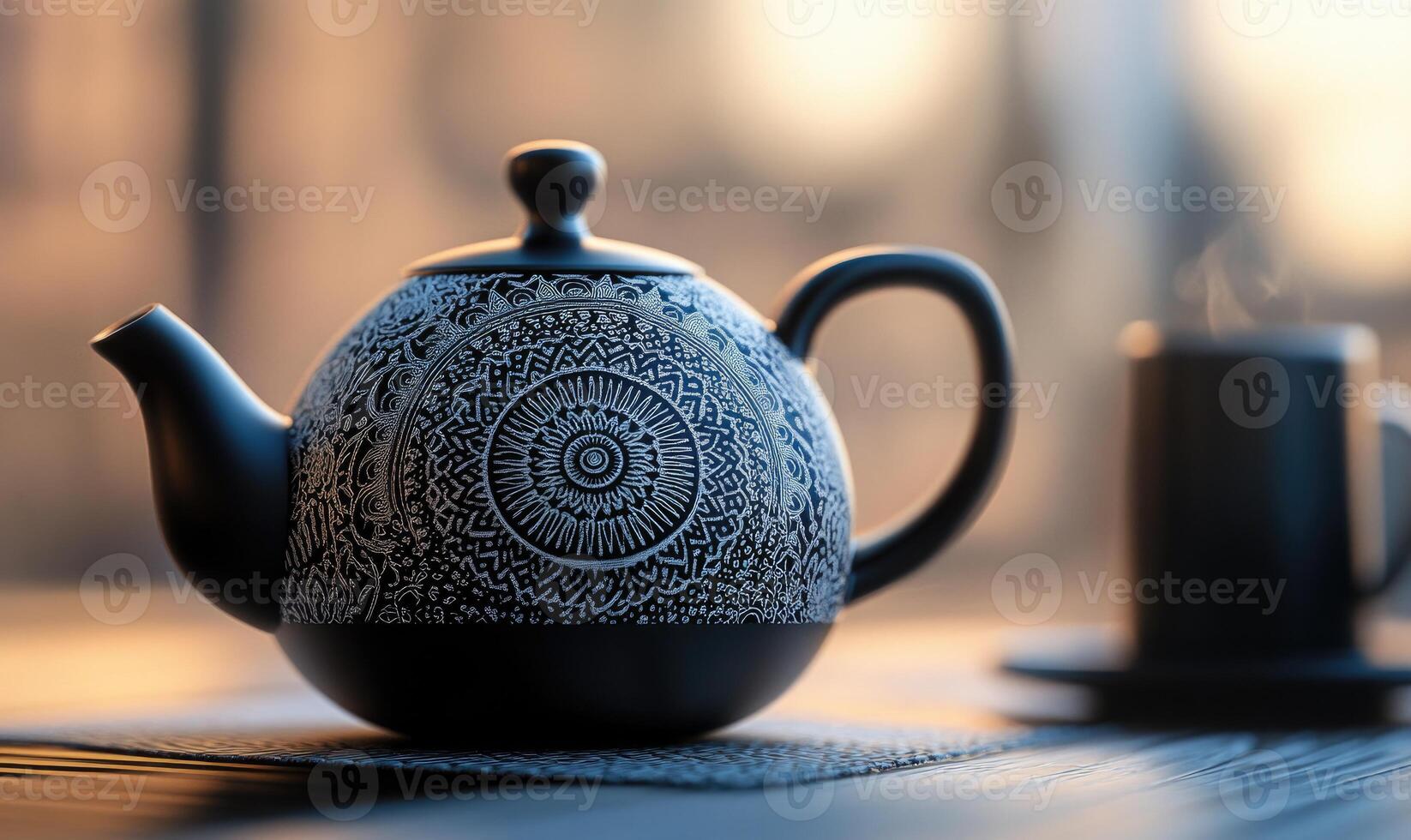 A black tea pot with a blue design sits on a table next to a cup of coffee photo