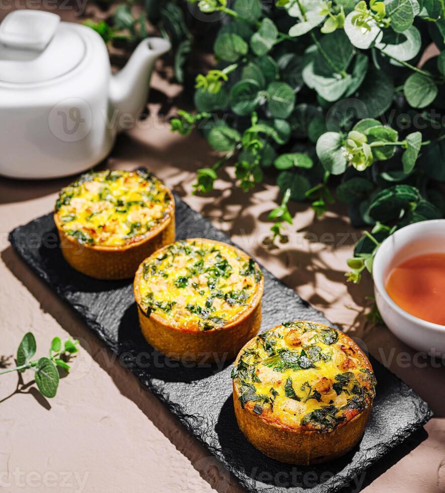 Savory mini quiches with spinach and herbs on a rustic table photo