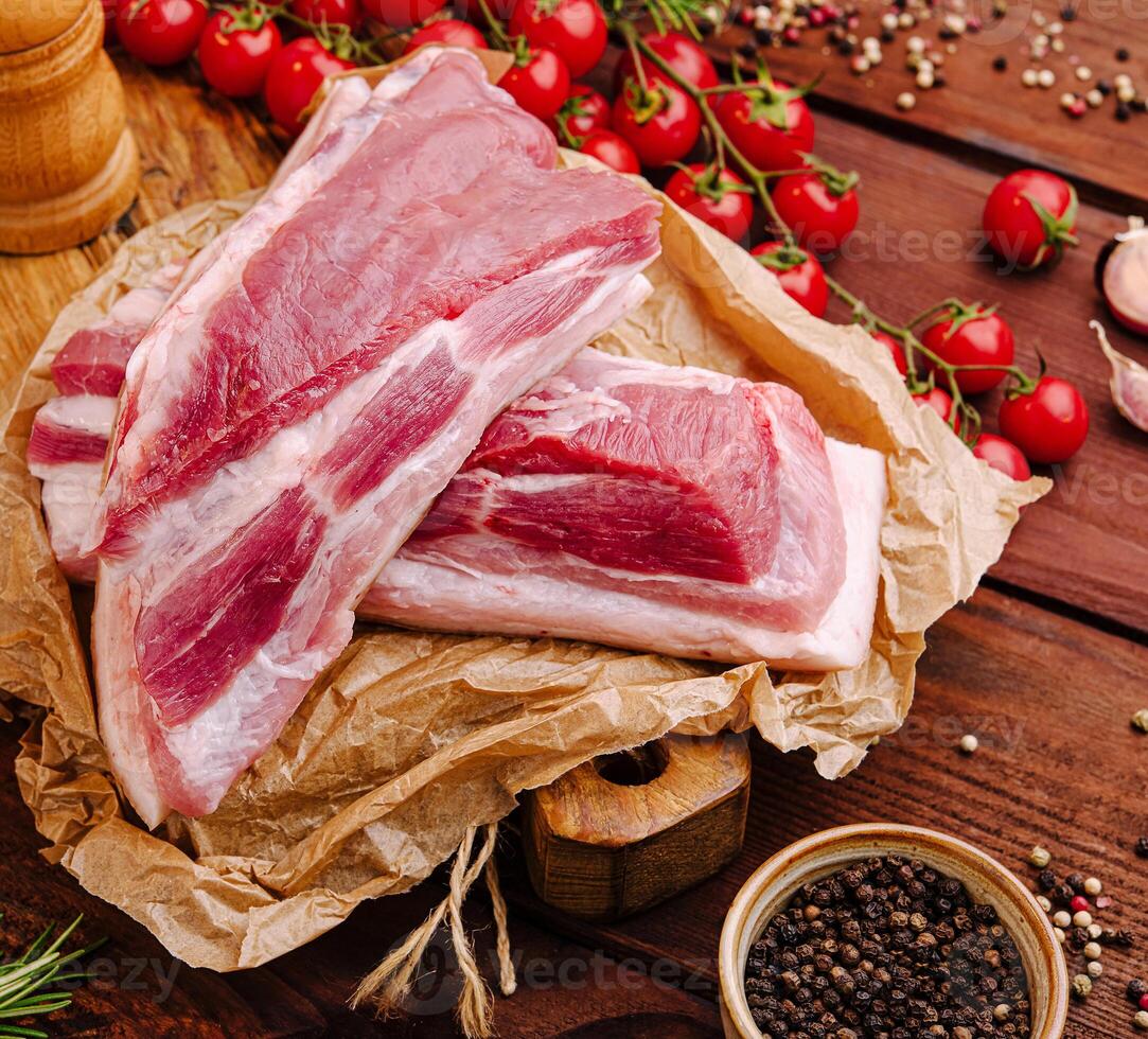 Fresh cuts of pork with herbs and cherry tomatoes on wooden surface photo