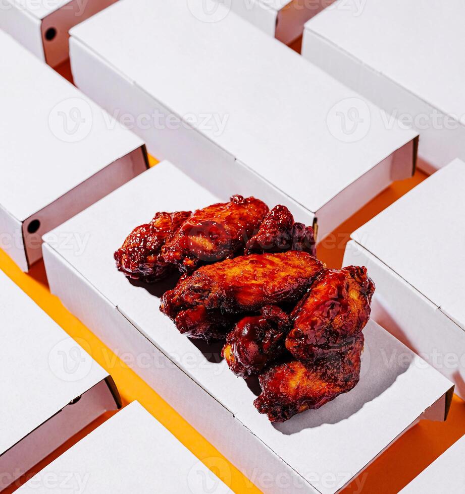 Juicy chicken wings in white boxes on an orange background photo