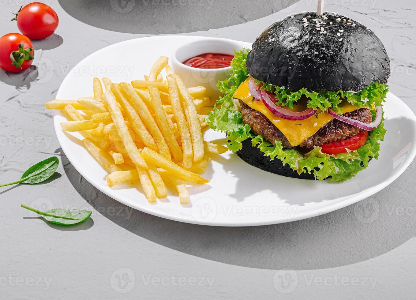 Black burger with golden fries and fresh tomatoes on a plate photo
