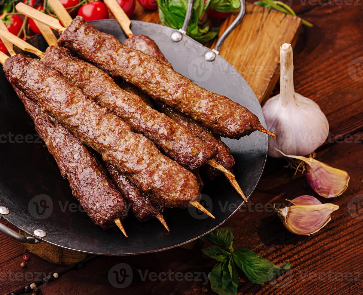 Grilled skewers of tender meat on a wooden table with vegetables photo