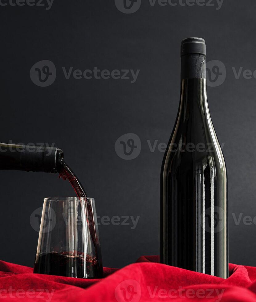 Pouring red wine into a glass beside a bottle on a velvet backdrop photo