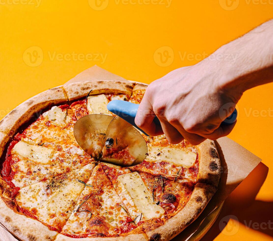 Hands using a pizza cutter on freshly baked pizza with cheese photo