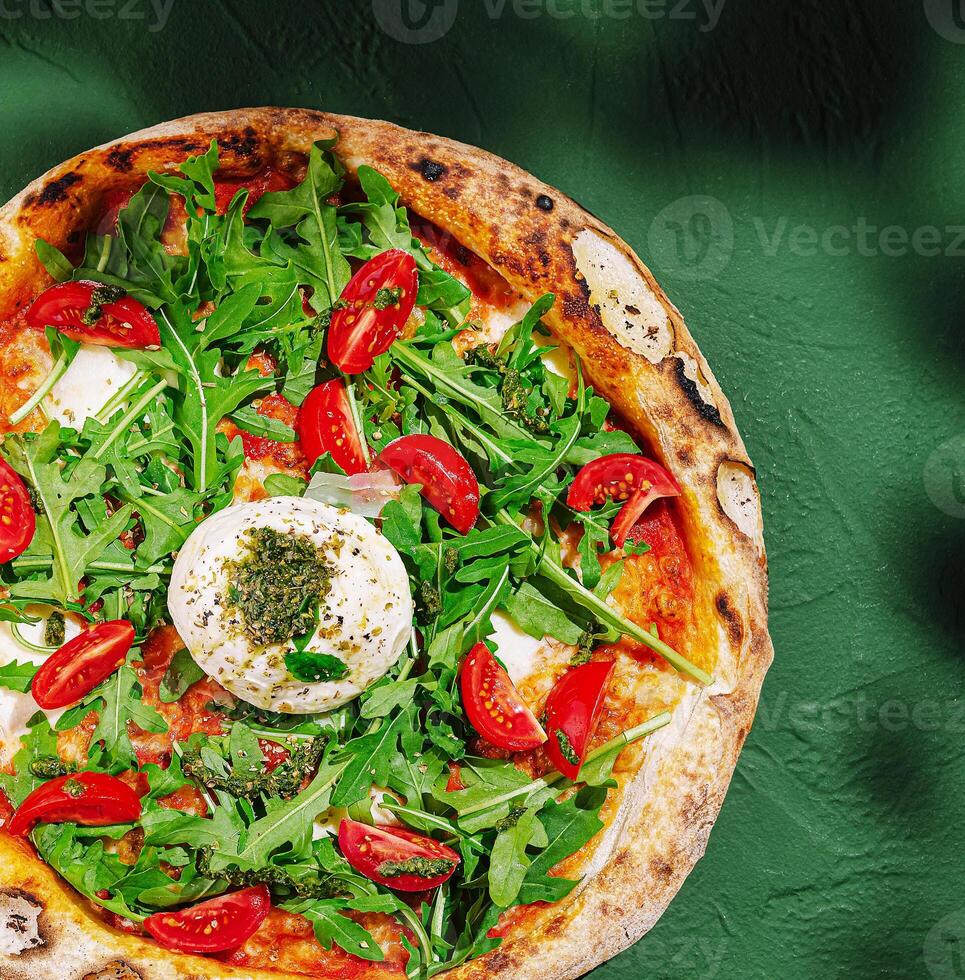 Fresh pizza topped with arugula and cherry tomatoes on a green table photo