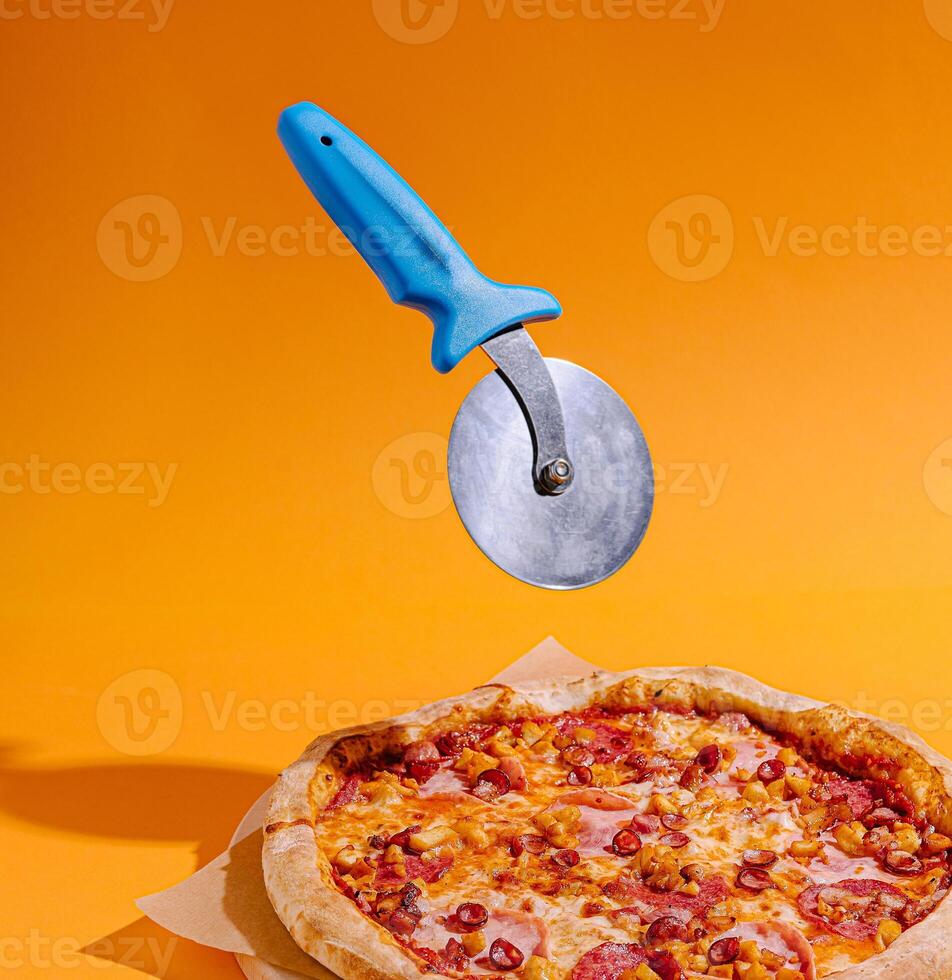 Pizza cutter hovering above a delicious pepperoni pizza photo