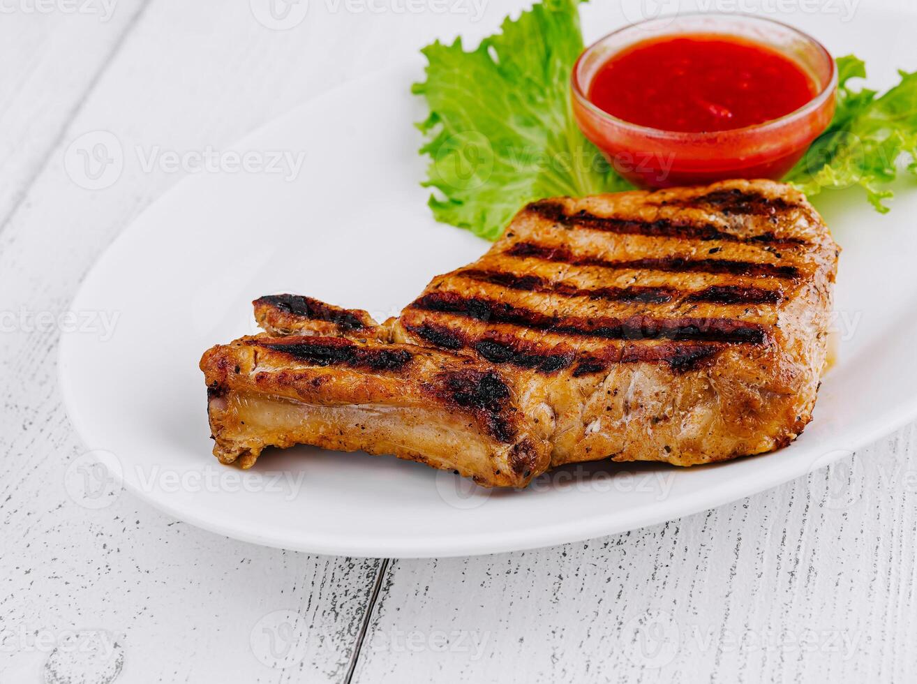 Grilled pork chop resting on white plate with lettuce photo