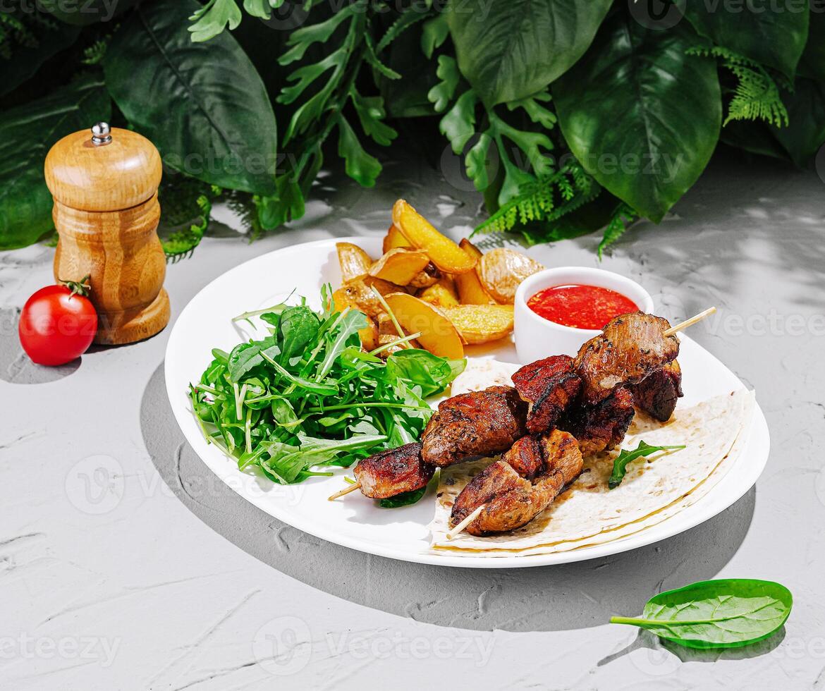 Delicious grilled skewers served with salad and potato wedges photo