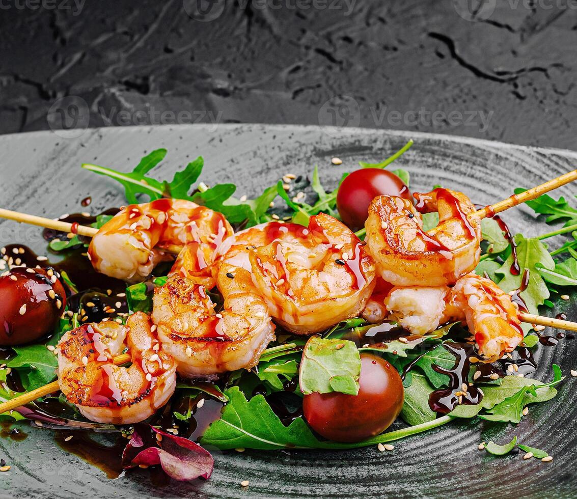 Grilled shrimp skewers served on fresh greens with sauce drizzle photo