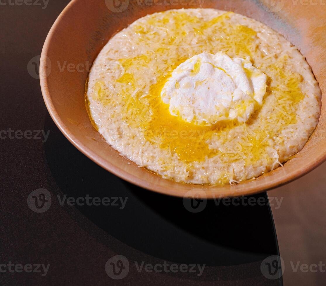 Creamy polenta being served with poached egg and grated cheese in a rustic bowl photo