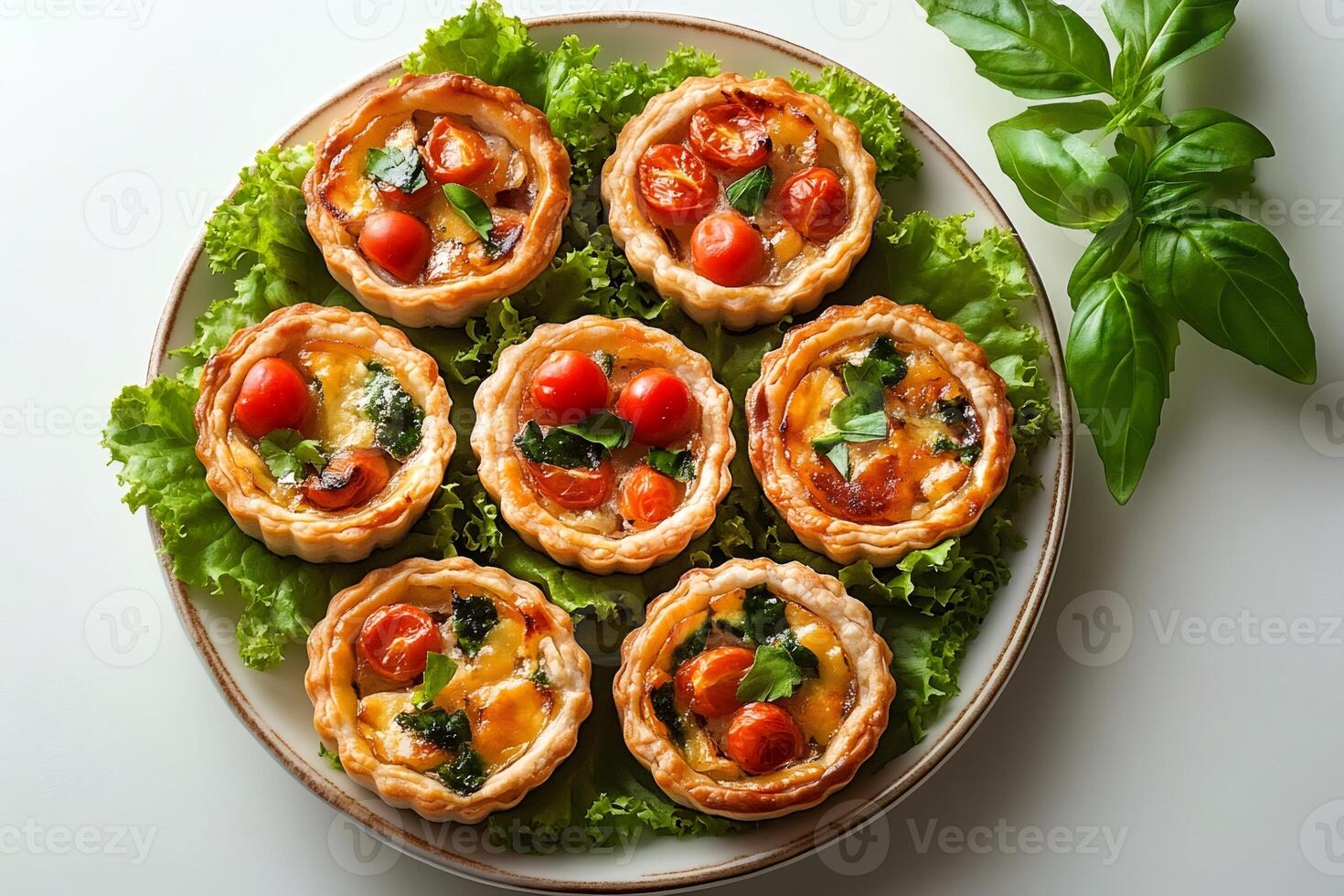 Mini quiches with cherry tomatoes, spinach, and basil resting on lettuce on a plate photo