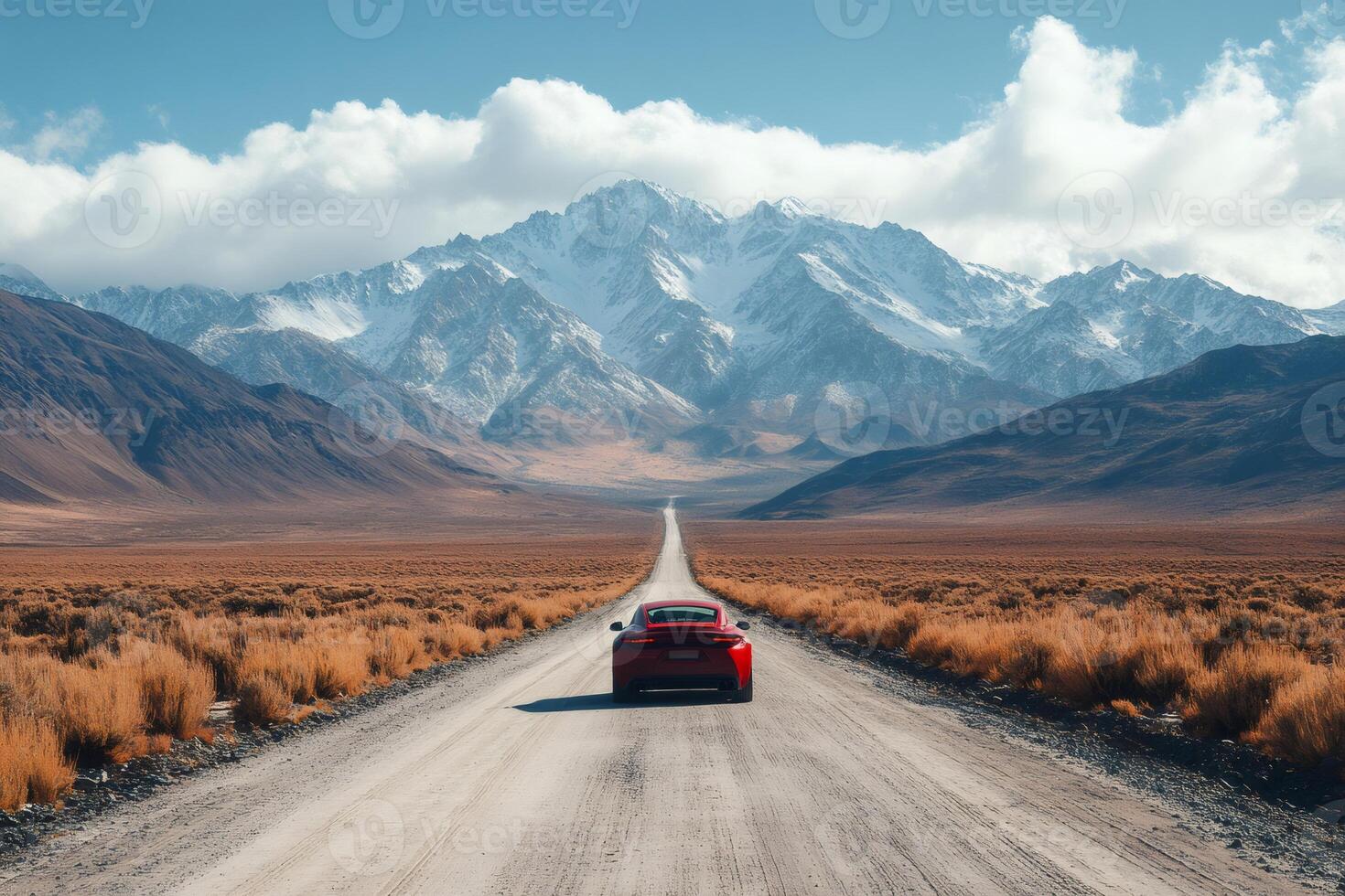 Red sports car driving on a long straight dirt road toward snowy mountains photo