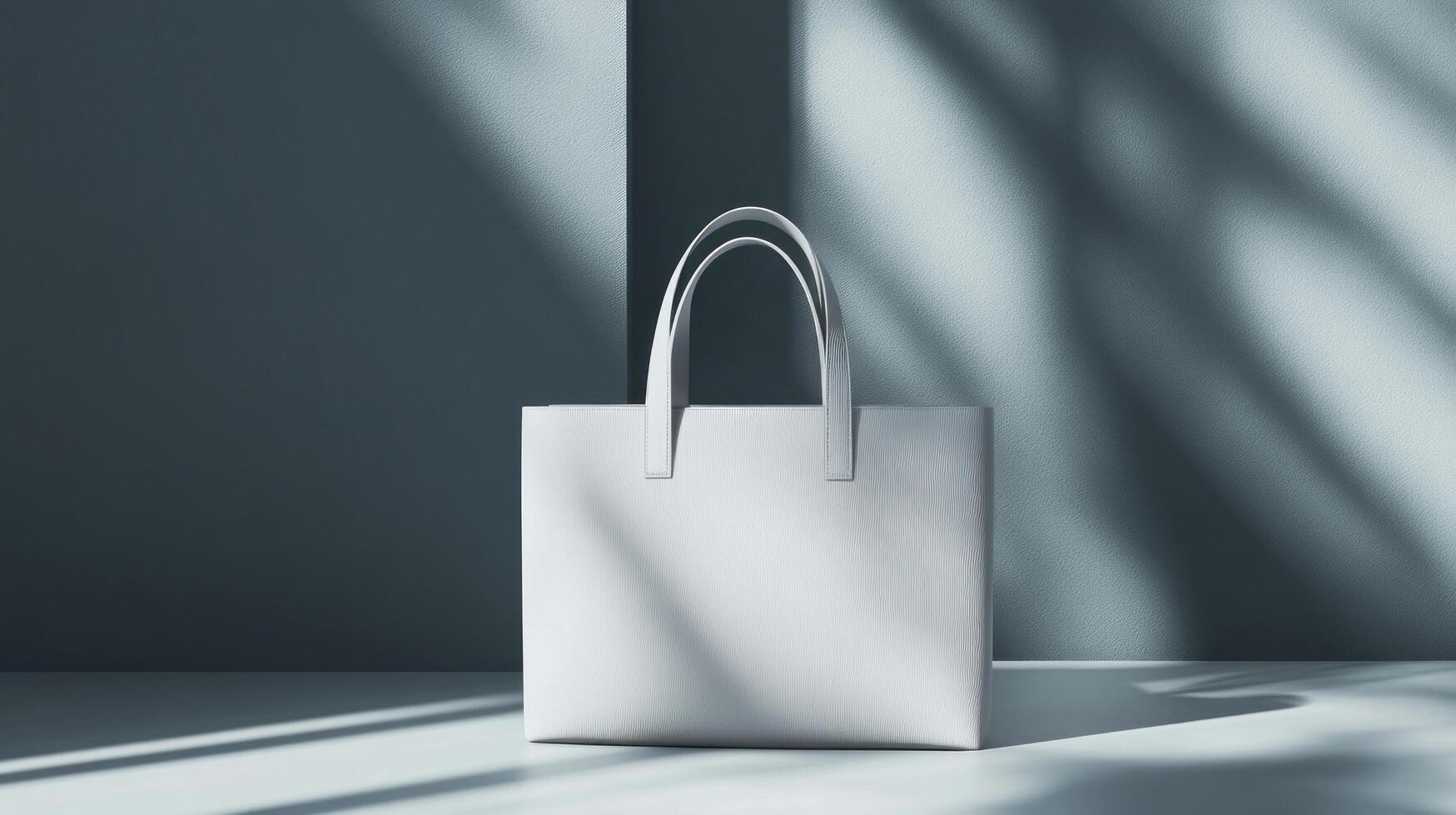 A minimalist white tote bag displayed against a muted, gray backdrop with dramatic shadows. photo