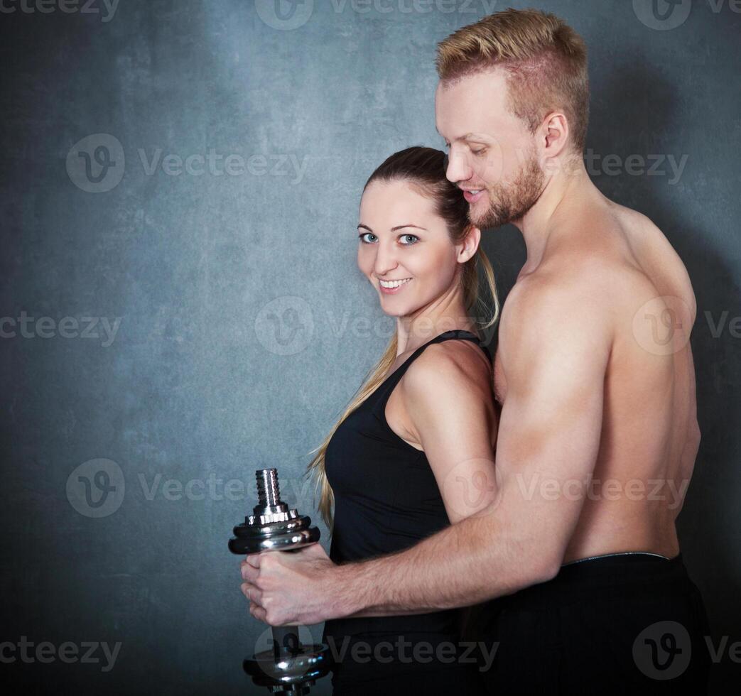 Athletic couple with a dumbells near the dark wall photo