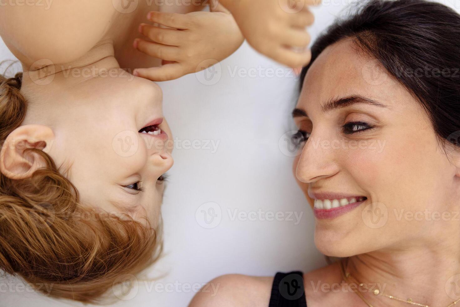 A close-up portrait in profile of a laughing mother and a cute child. A smiling woman and her little son are lying on a white floor. photo