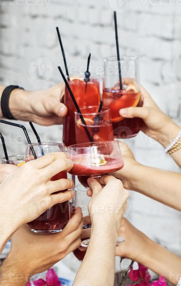 Close-up of male and female hands with elegant glasses. Men and women toast with goblets of delicious fragrant cocktails. Friends clink glasses with tasty drinks. photo