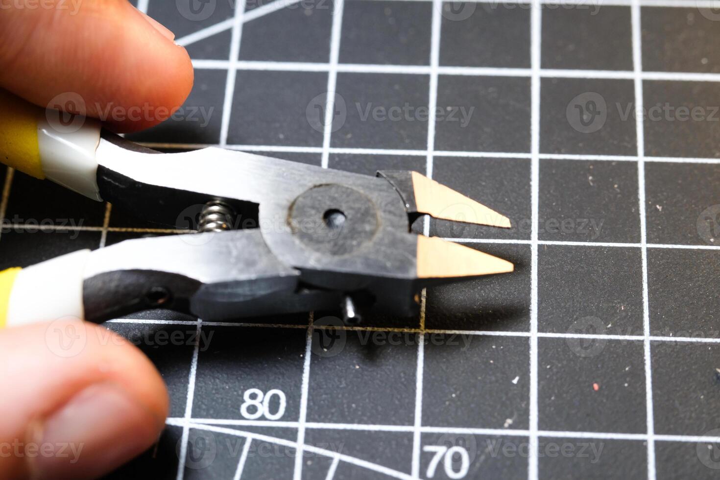 Fingers holding stainless nipper for cutting plastic. Black Cutting mat background with white lines. The concept of a master model kits hobby. Negative space. Sharp pliers photo