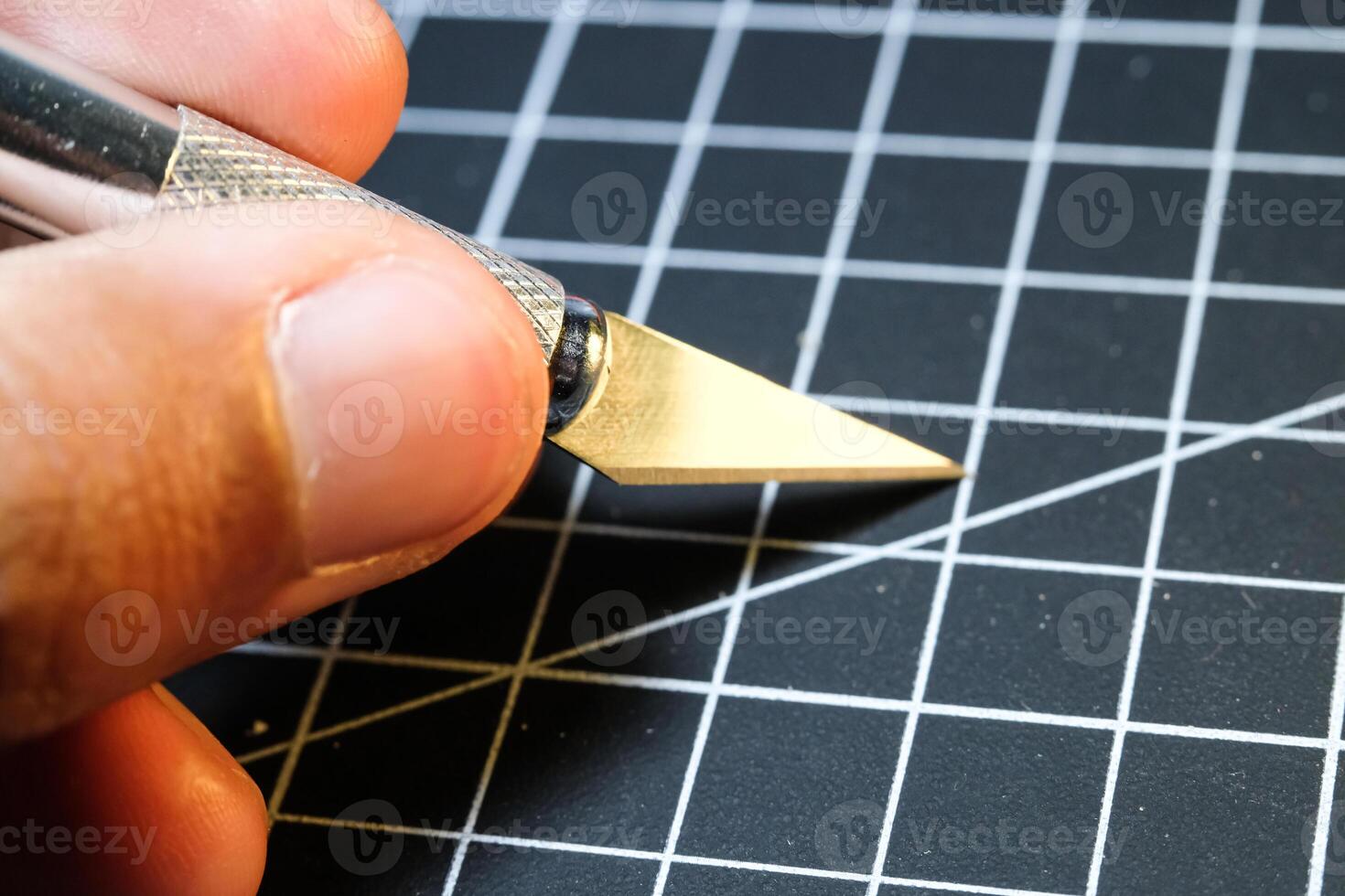 Closeup of a hand holding a cutting pen on black striped rubber mat. Sharp cutting blade used to cut plastic parts. Metal tools and equipment. Tools for hobbyist robot model kit. photo