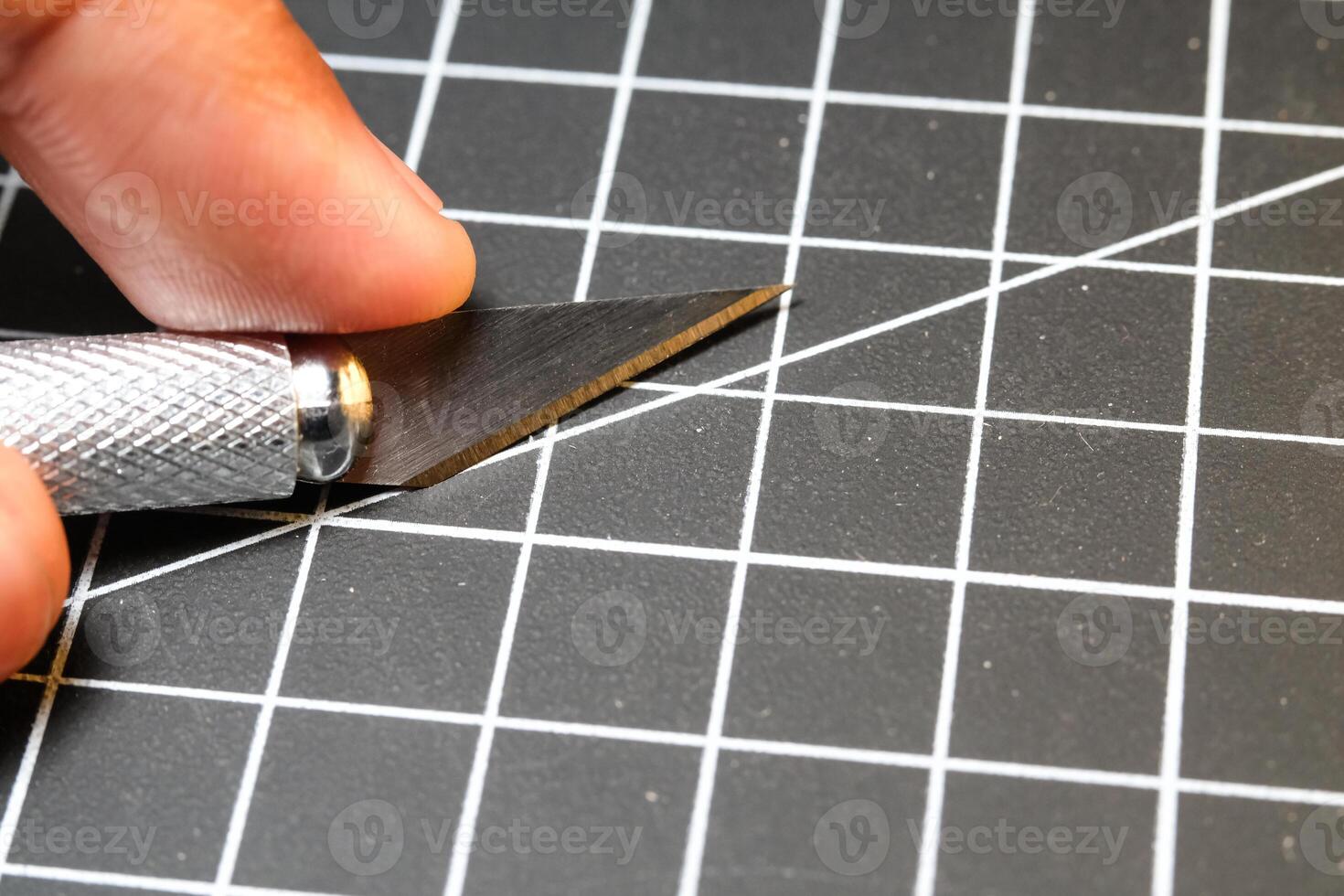 A hand holding a cutting pen on black striped rubber mat. Sharp cutting blade used to cut plastic parts. Metal tools and equipment. Tools for hobbyist robot model kit assembly. photo