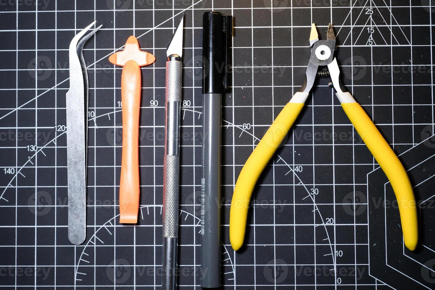 Tools set for building plastic model kits. Consisting of Nipper, Ink pen, cutting blade, plastic separator, and metal tweezer. Tools and equipment on black cutting mat. Toys and Model kits photo