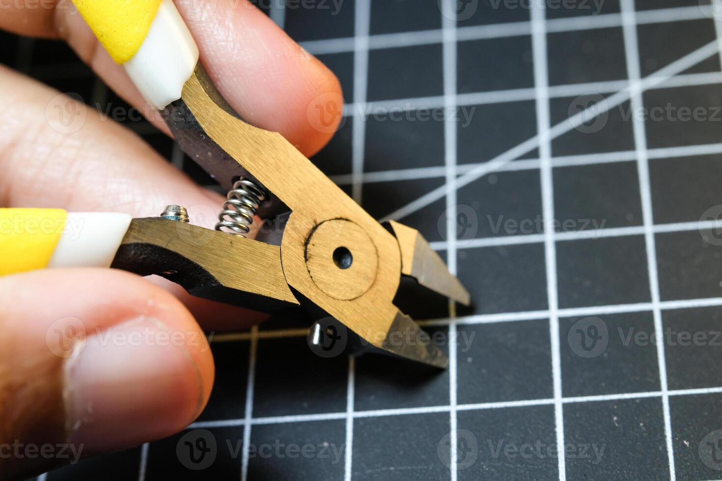 Closeup of fingers holding stainless nipper for cutting plastic. Black Cutting mat background with white lines. The concept of a master model kits hobby. Negative space. Sharp pliers photo