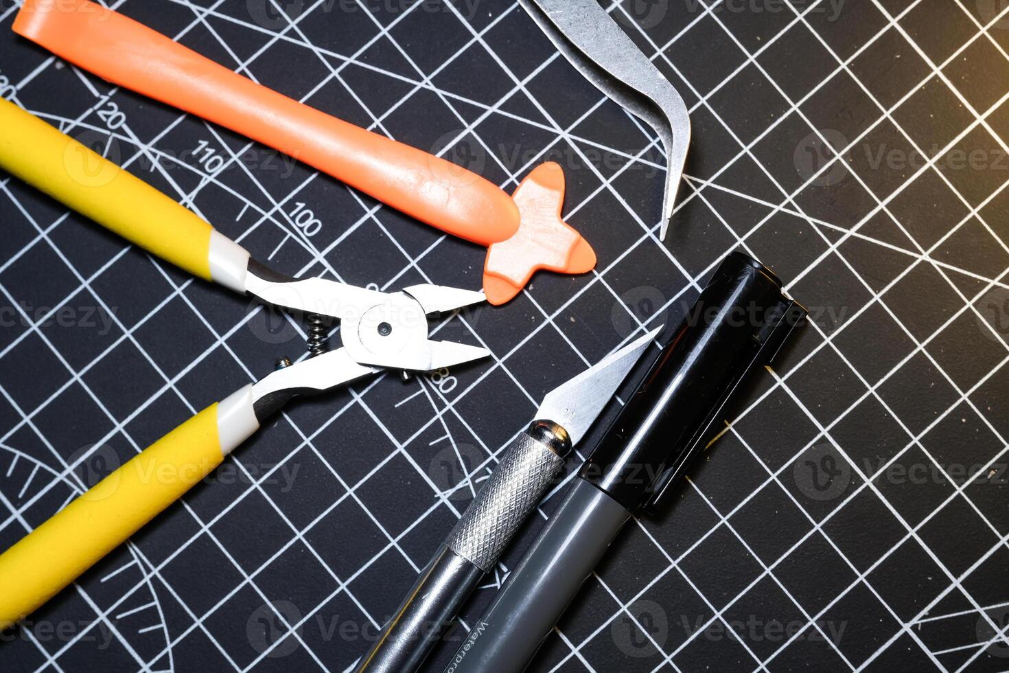 Tools set for building plastic model kits. Consisting of Nipper, Ink pen, cutting blade, plastic separator, and metal tweezer. Tools and equipment on black cutting mat. photo