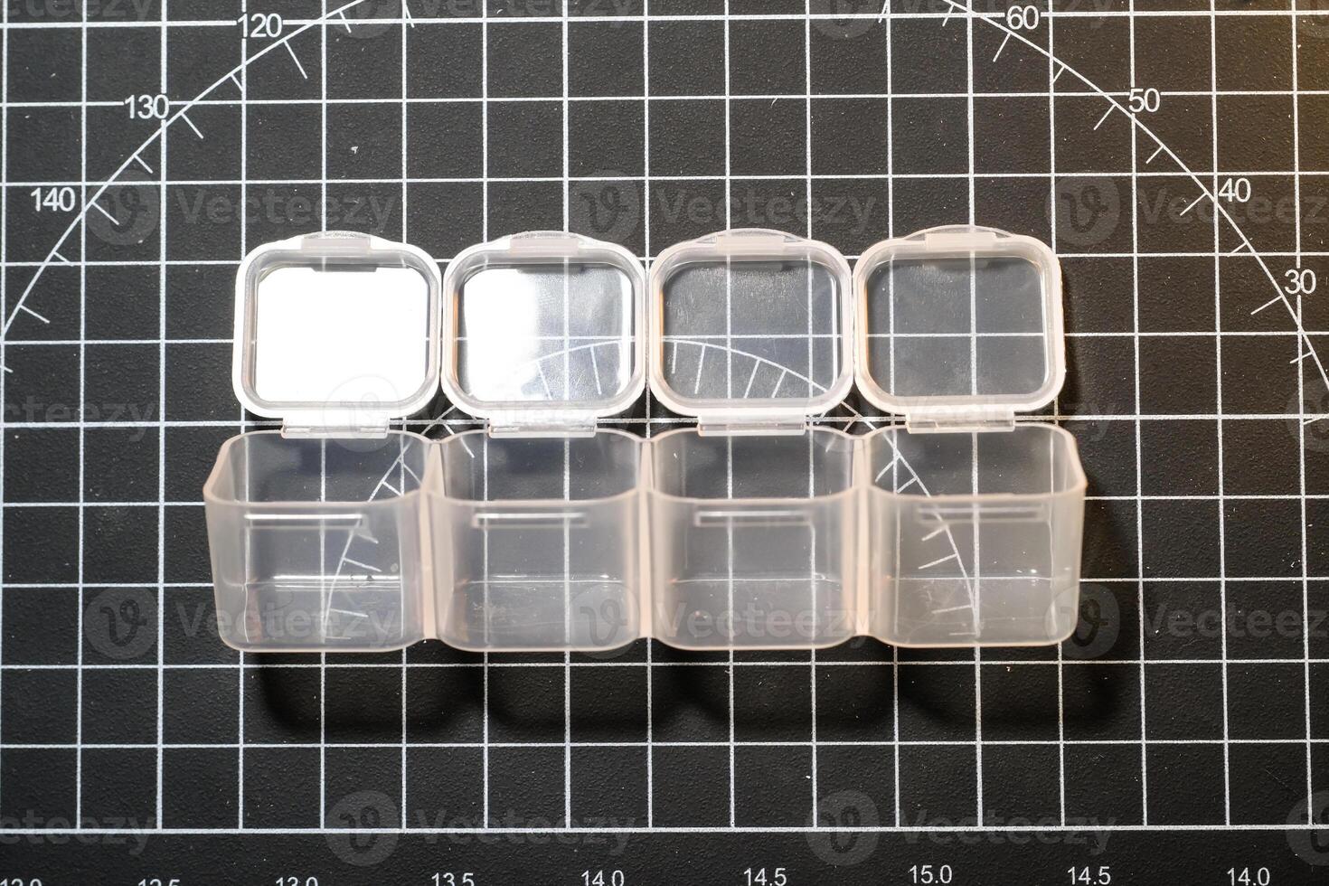 Mini transparent container on black striped cutting mat. Four small containers for storing tiny parts. Model kits and robotic build hobbies. Plastic equipments. Isolated objects on black backgrounds photo