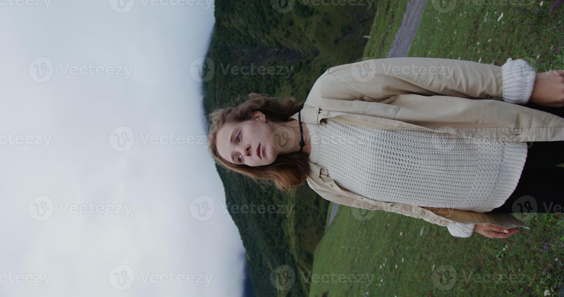 Caucasus, Elbrus. A young woman of European appearance with hiking hat, dressed in warm sweater and jacket, looks around while standing among the mountains covered with thick forest. Vertical photo