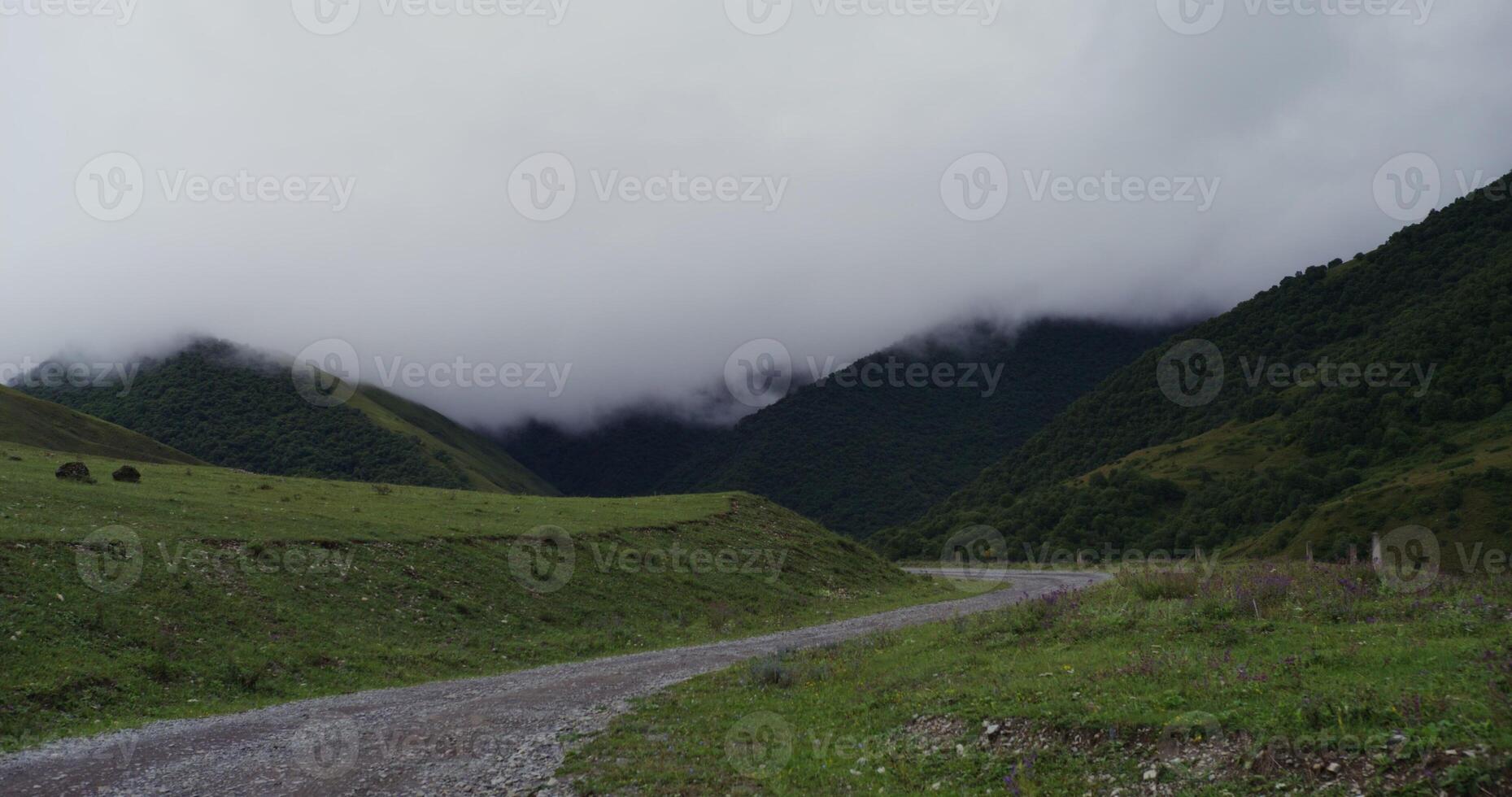 Mountain road among the grassy slopes. The tops of the mountains are covered with fluffy clouds photo