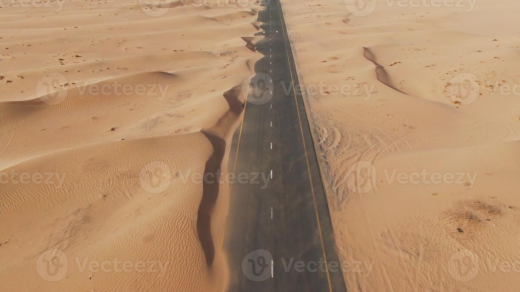 Aerial view of desert paved road buried by sand dunes. Dubai, United Arab Emirates. Daylight drone shooting. Rare cars drive down the road photo
