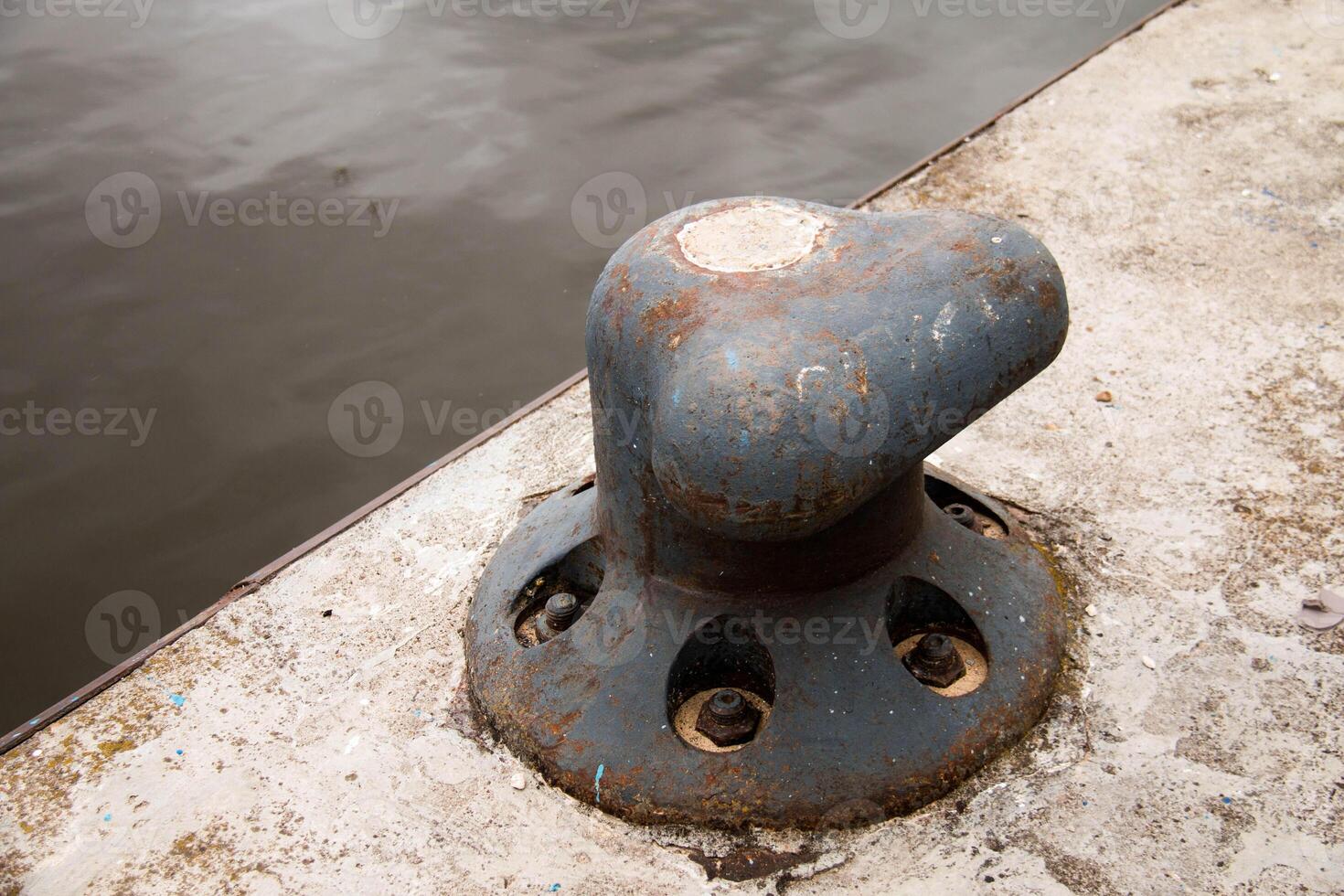 Rustic Metal Mooring Bollard mounted on Concrete Pier water, providing secure Docking for Boats. Weathered metal, aged surface, industrial setting emphasize functional enduring nature infrastructure photo