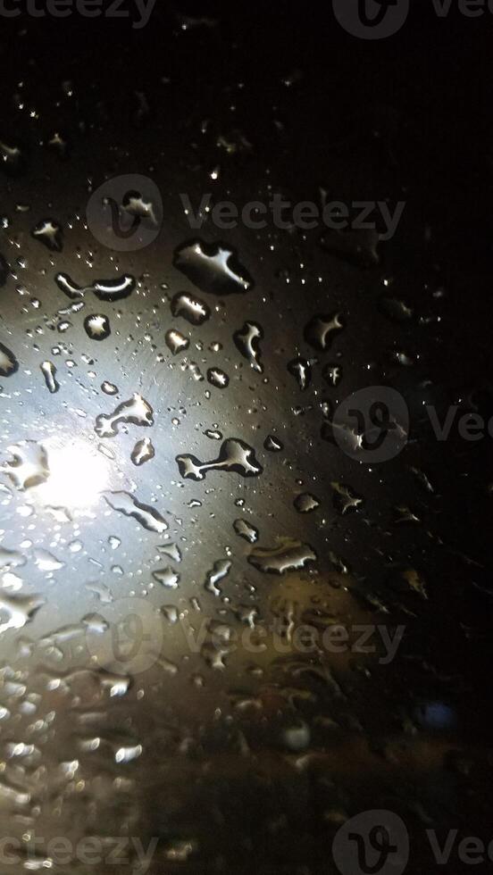 Rain Droplets at Night on Wet Windshield Near Streetlight photo