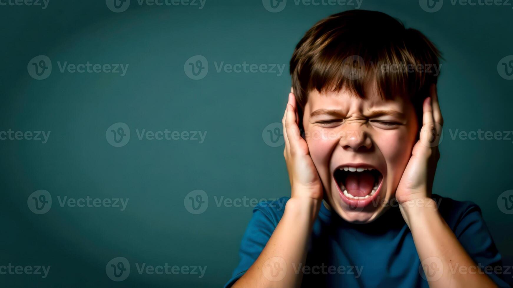 A portrait of a dark-haired boy screaming and covering his ears with both hands, on dark green background with empty space for text on the left, for banners, cards or messages photo