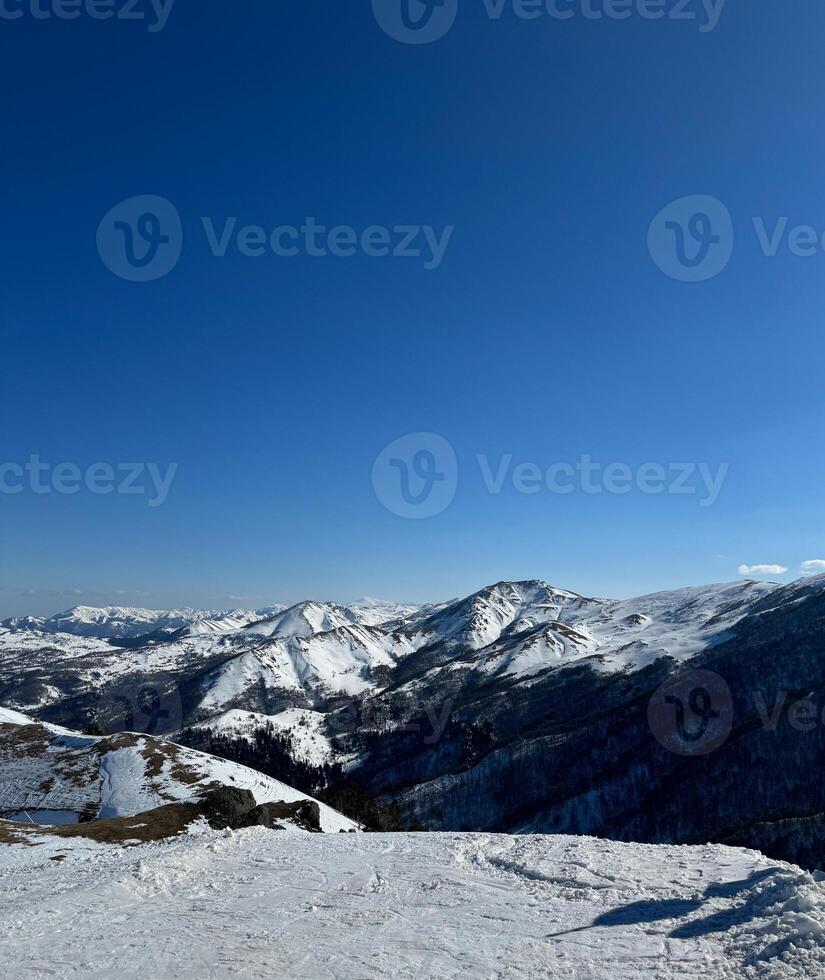 Vertical aerial view of the snow-covered mountain peaks in Bakuriani, Georgia, clear blue sky, with space for text, for cards and banner photo