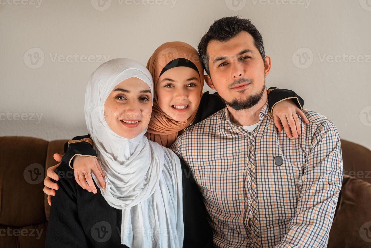 Portrait of a happy Muslim family at home, a young father, mother and child daughter in hijab looking at the camera and smiling. photo