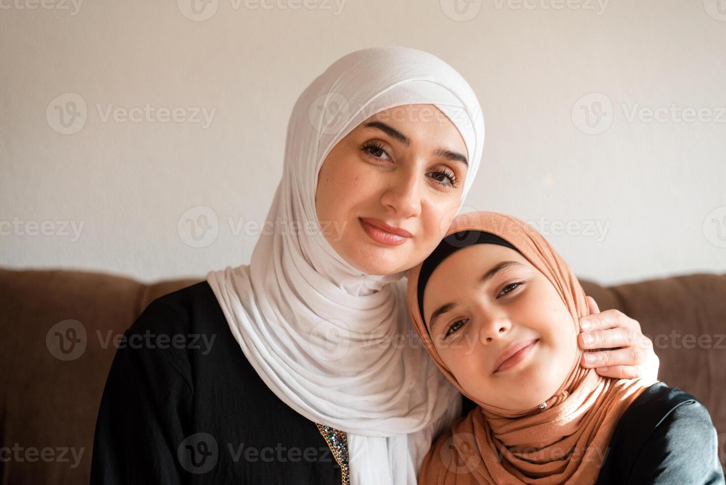 Portrait of a happy Muslim family at home young mother and child daughter in hijab looking at camera and smiling. photo