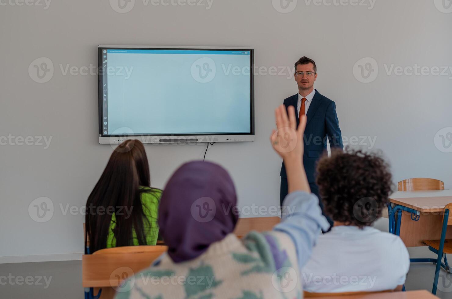 In the classroom group of college students listening to a university lecturer and engages in discussion and debate. Student raising a hand with a question for the teacher. photo