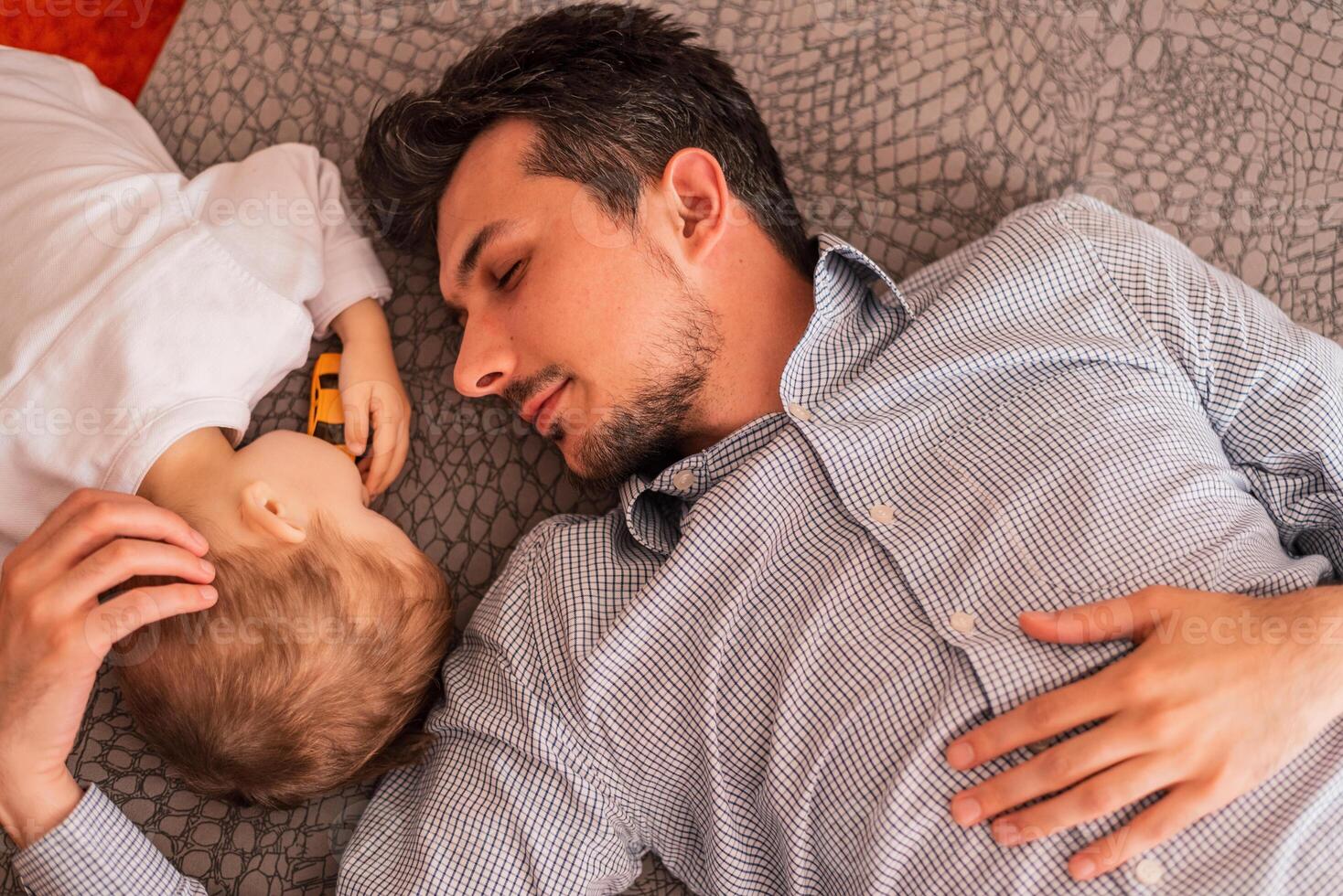 A young father shares love with his son and spends time together at home, lying and sleeping on the bed, top view. photo