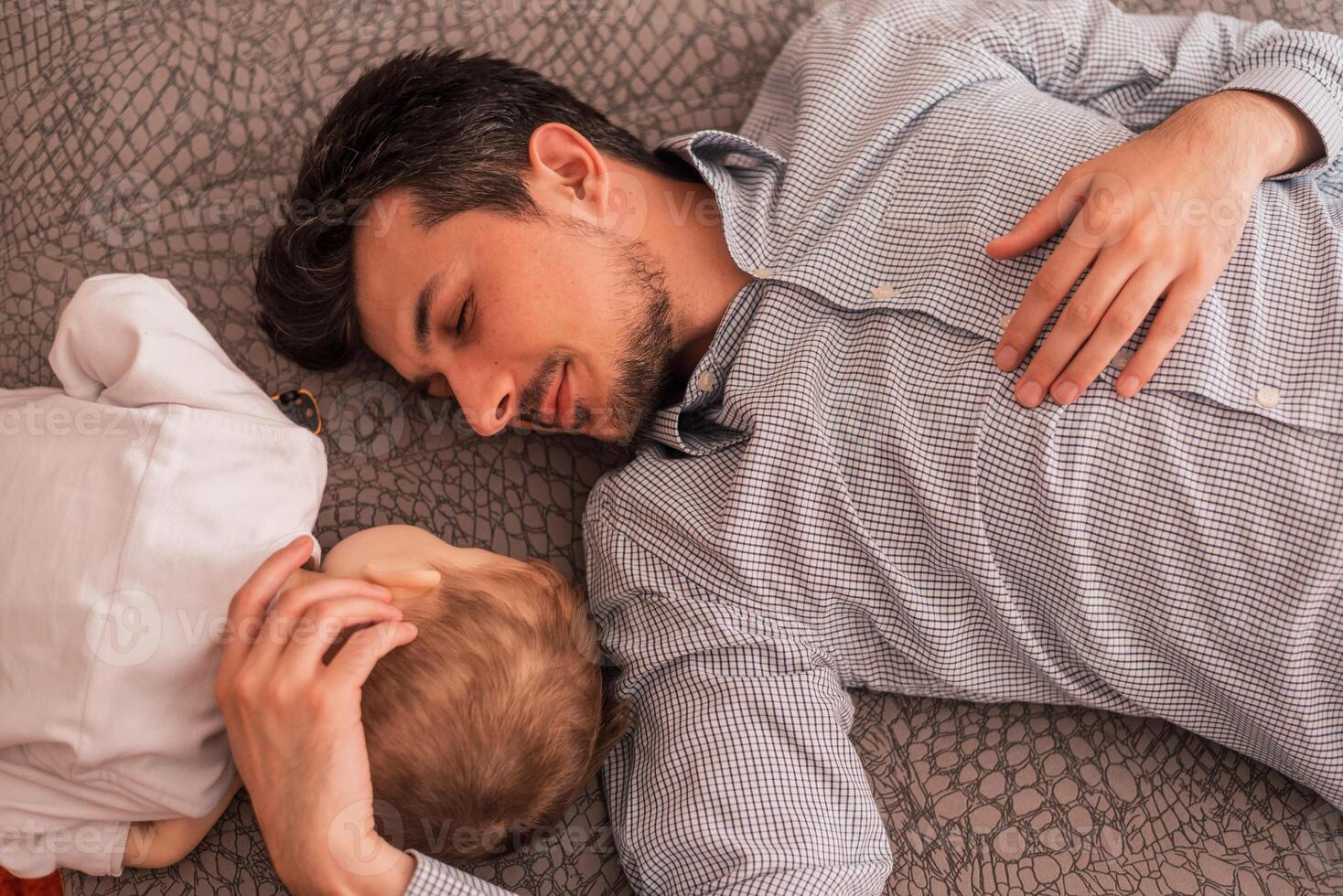 A young father shares love with his son and spends time together at home, lying and sleeping on the bed, top view. photo