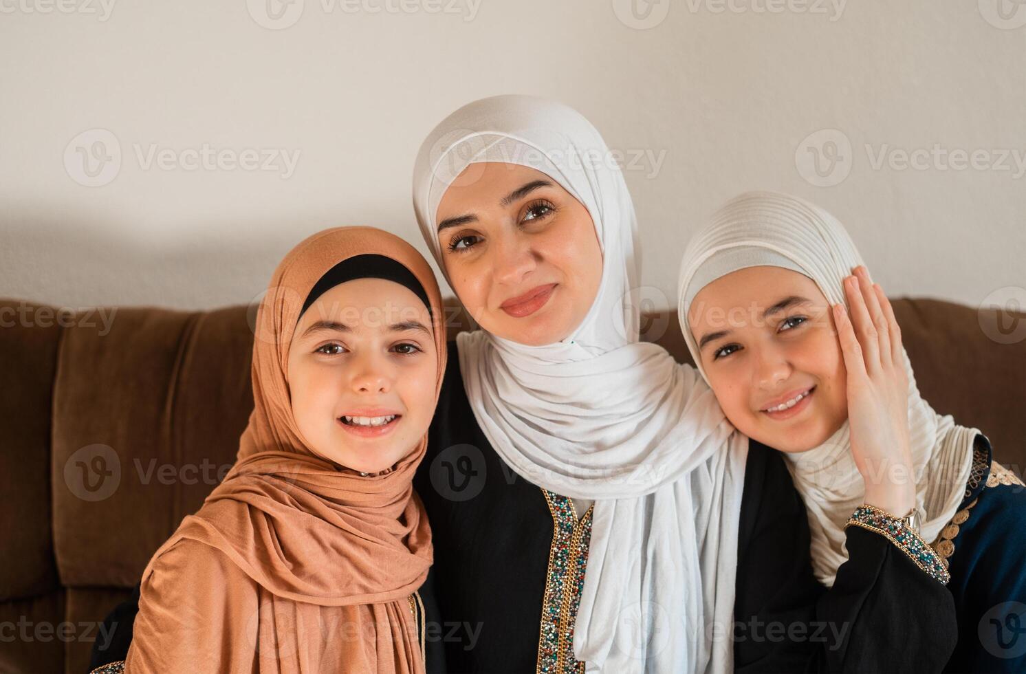 Portrait of a happy Muslim family at home, a young mother and two child daughters in hijab looking at the camera and smiling on mother day. photo