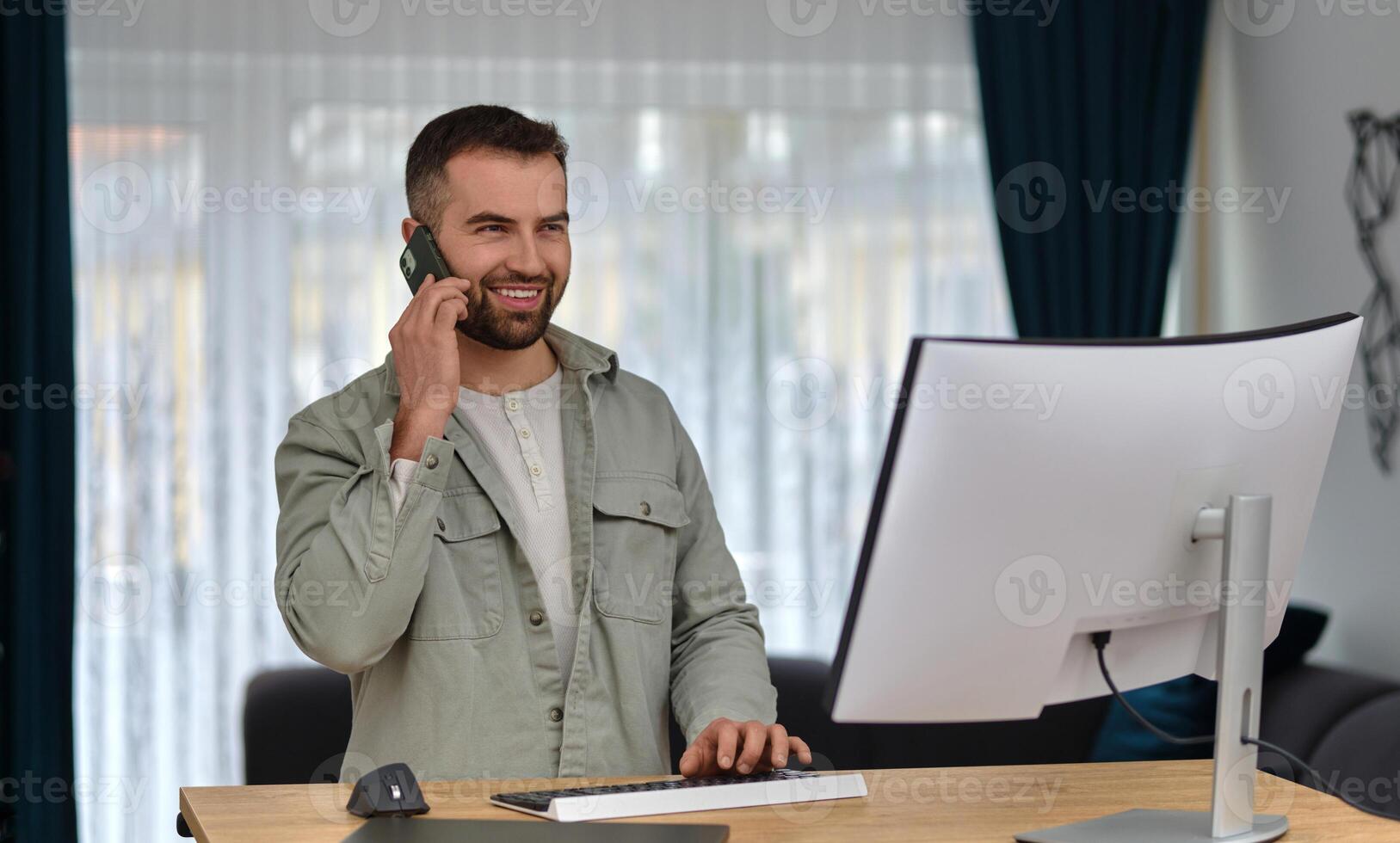 A young happy man talking on his phone while working at home office. photo