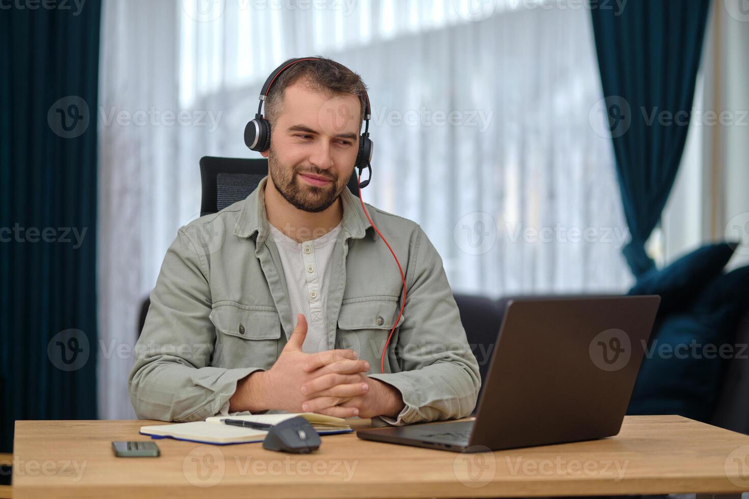 A happy man working at home office, wearing wireless headphones, having a call with clients on a laptop, customer service or contact us support photo