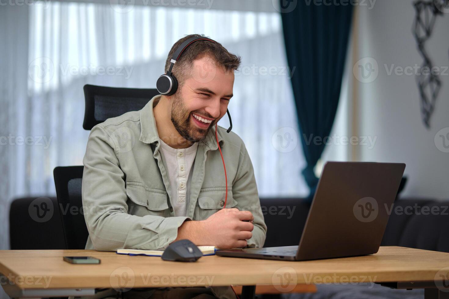 A happy man working at home office, wearing wireless headphones, having a call with clients on a laptop, customer service or contact us support photo