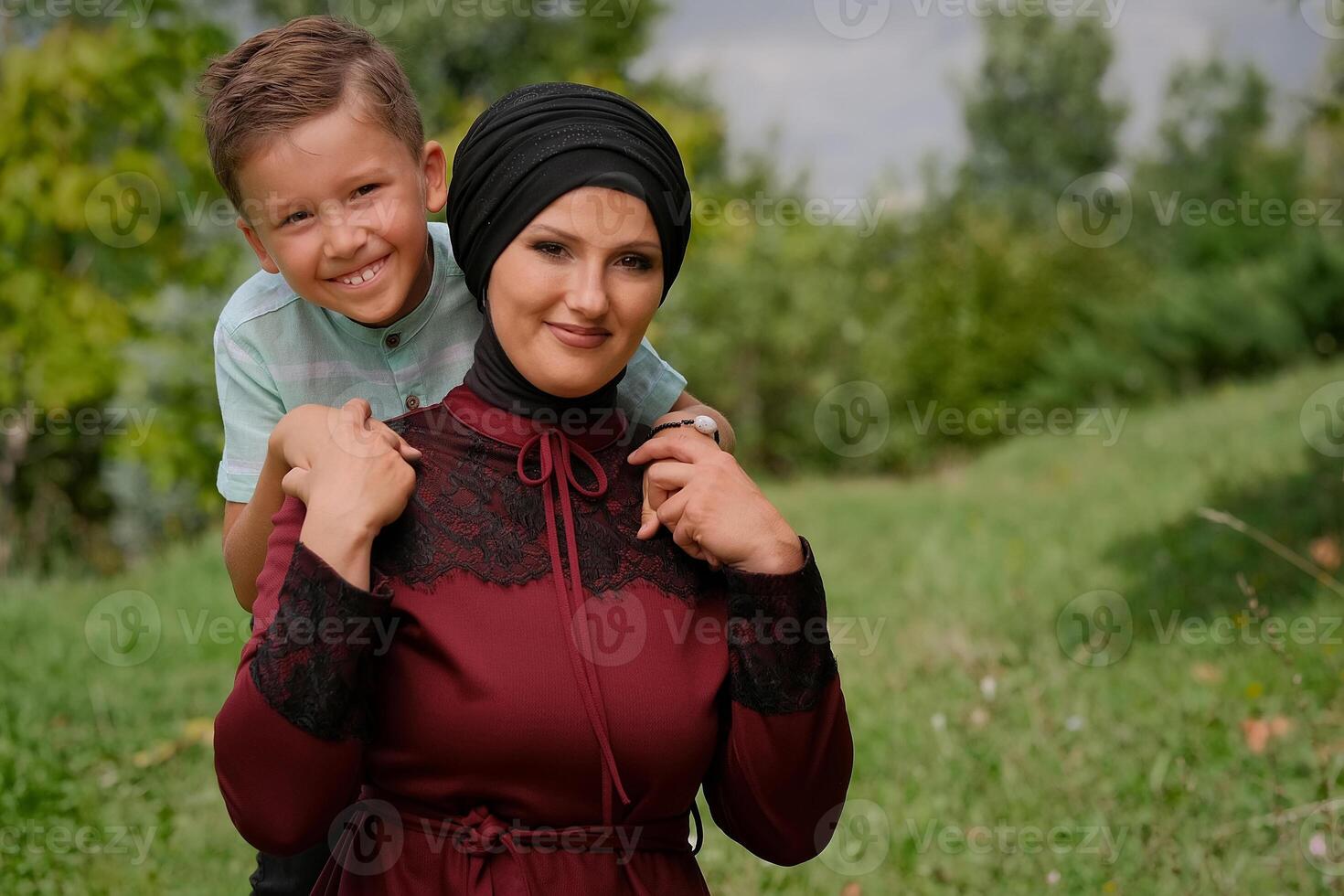 Portrait of happy Muslim family outside, mom and child son hug with love in summer park, looking at the camera and smiling.. photo