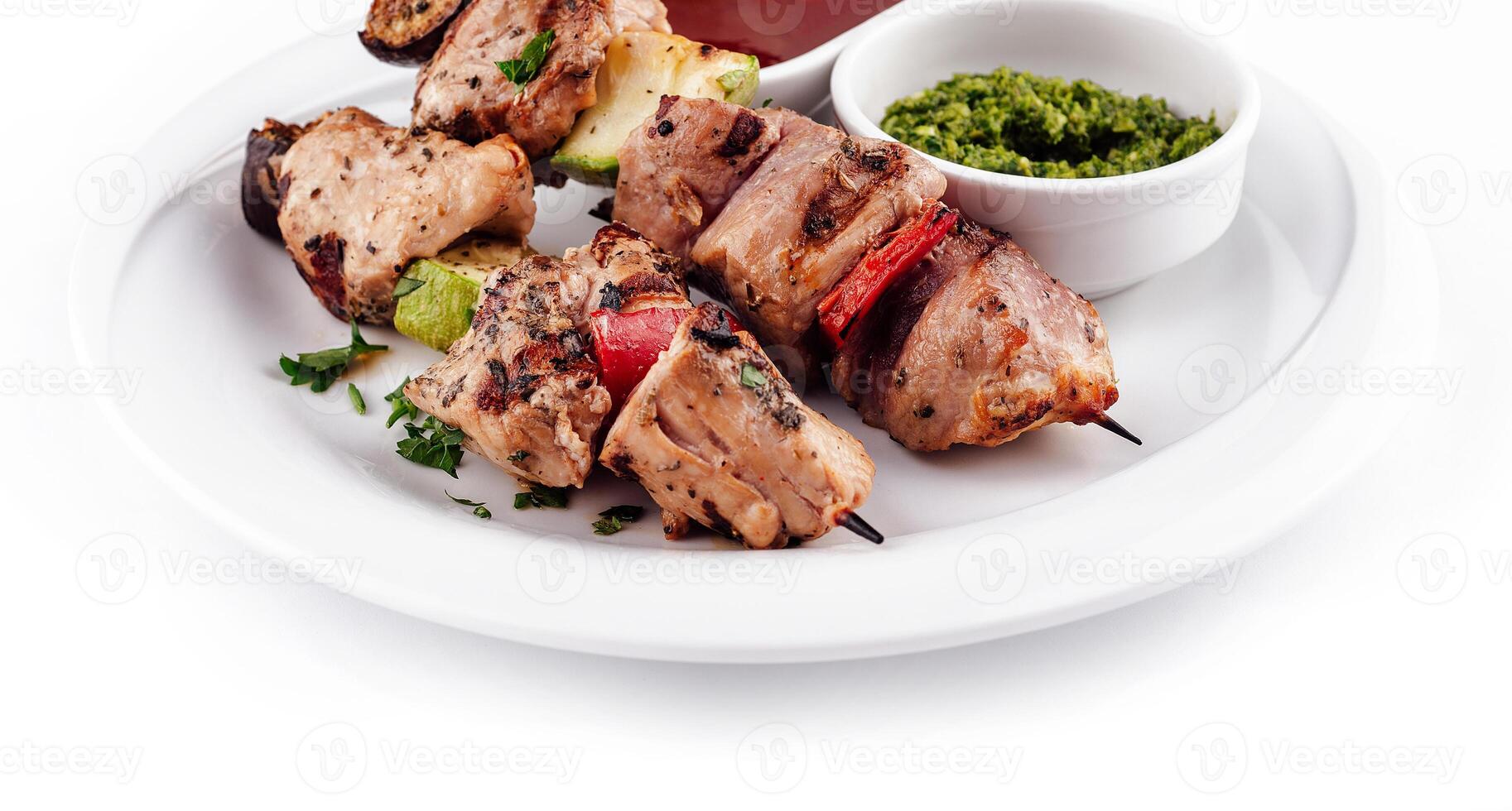 Grilled meat and vegetables on skewers served on white plate with sauces photo