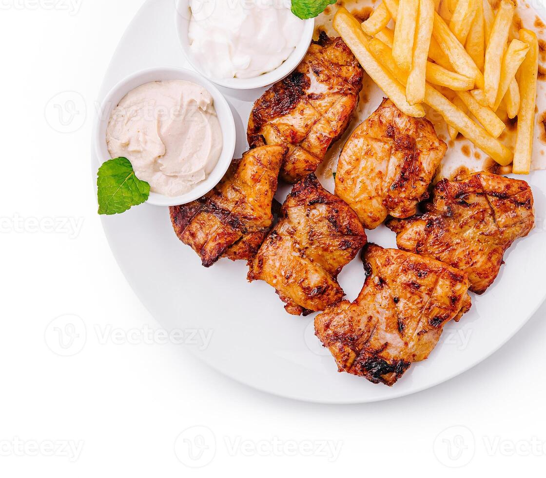 Grilled chicken with fries and dipping sauces on a white plate photo