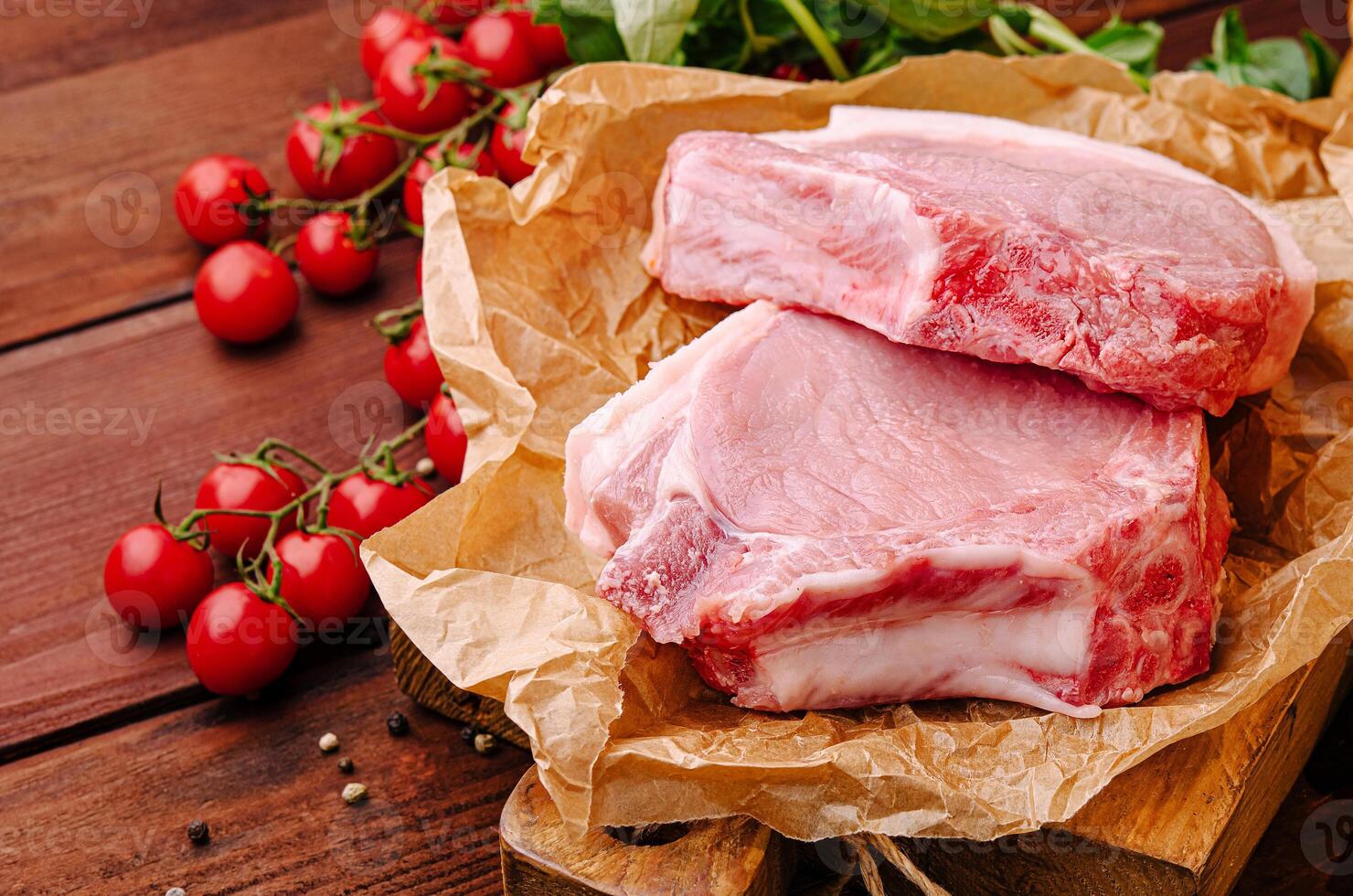 Fresh pork chops with cherry tomatoes and herbs on wooden board photo