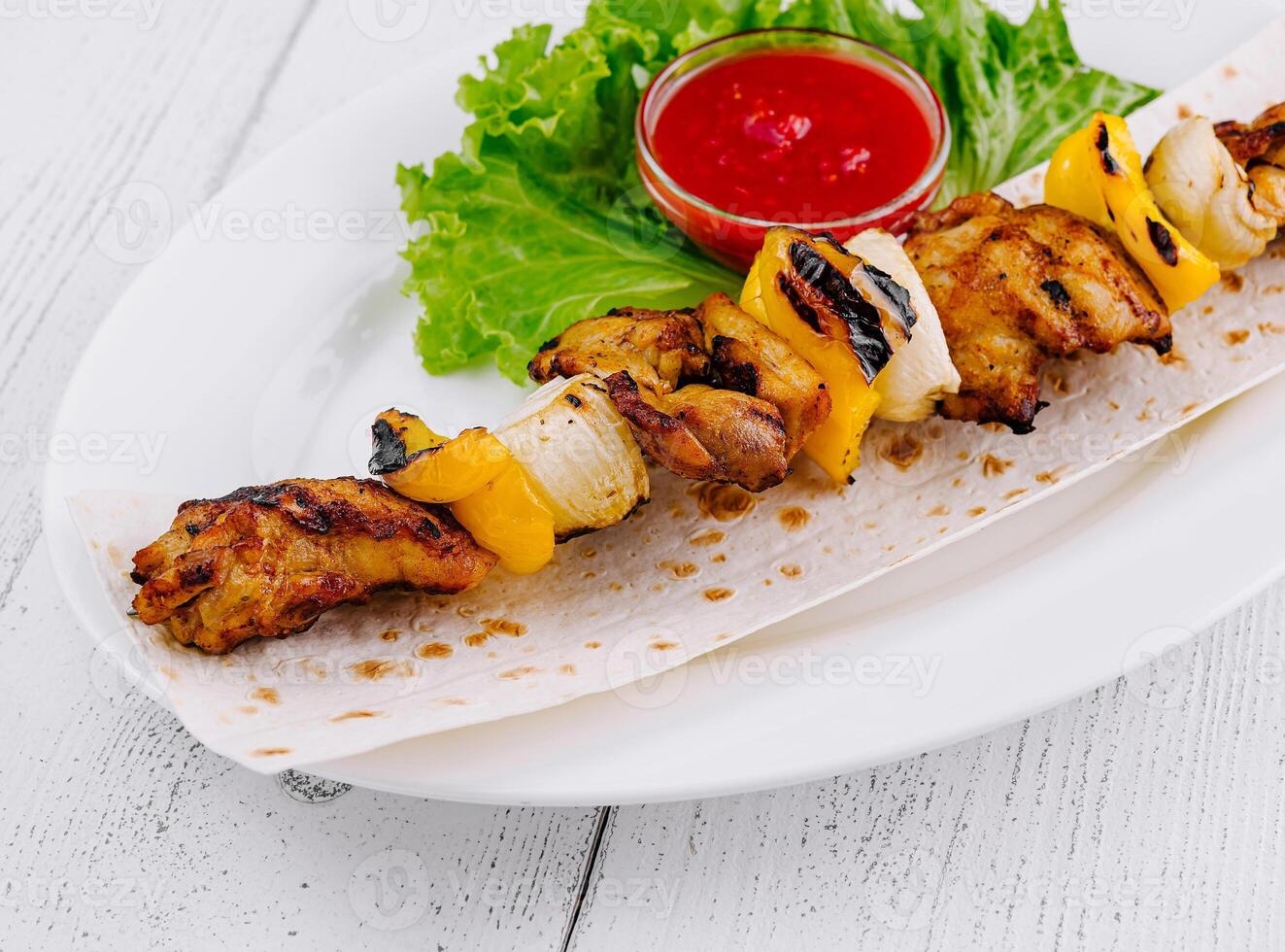 Grilled chicken shish kebab served on pita bread with tomato sauce and lettuce close up photo