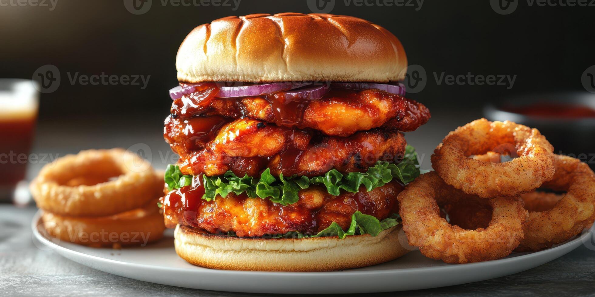 Juicy chicken sandwich stacked with crispy onion rings and barbecue sauce served on a white plate photo