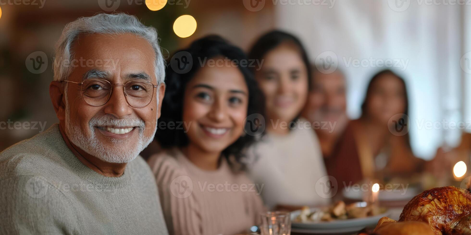 An older man is smiling at the camera while sitting at a table with his family photo
